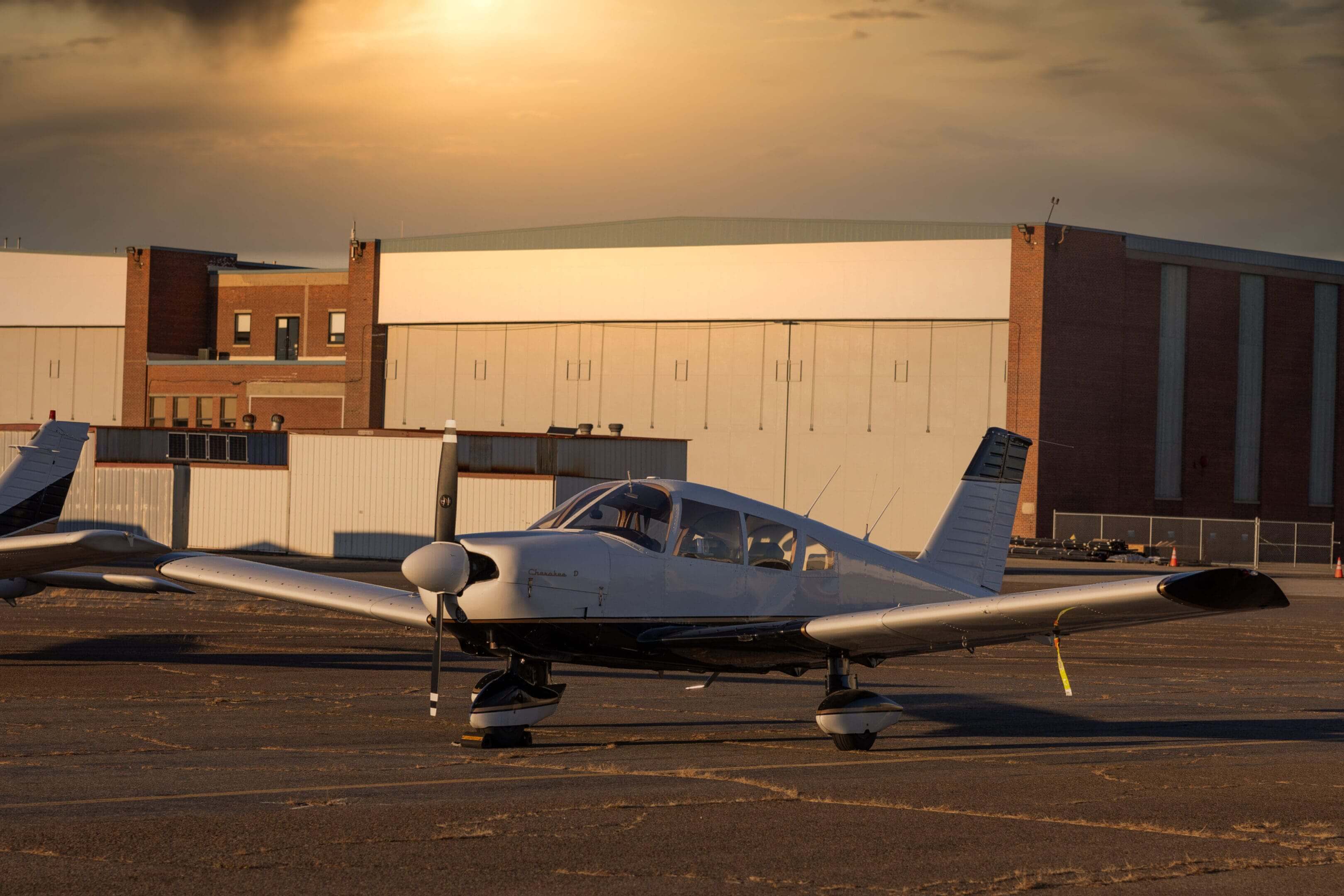 Small airplane parked near large hangars.
