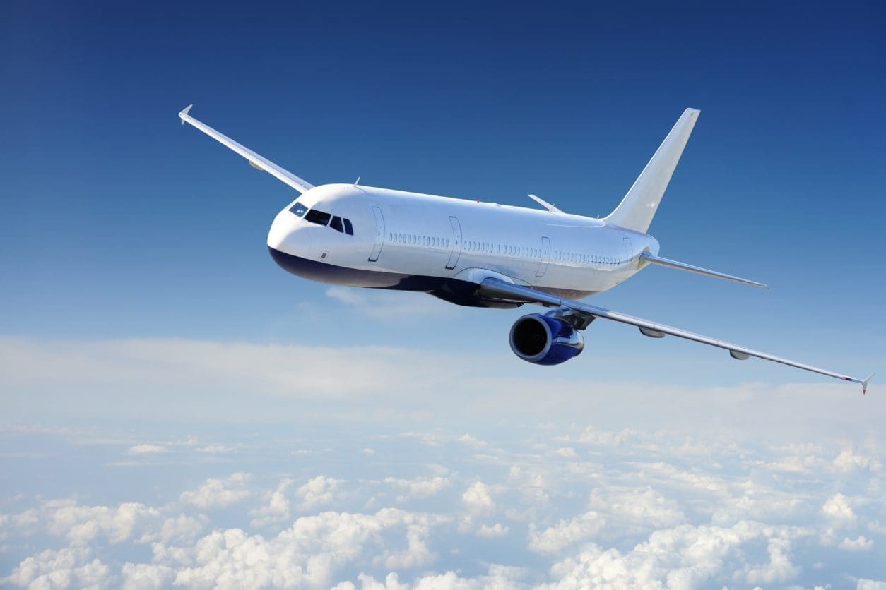 A commercial airplane flying above the clouds in a clear blue sky.