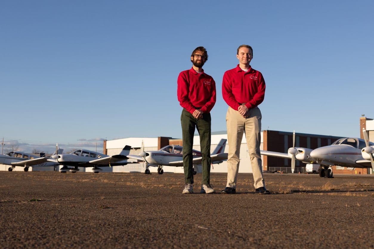 Two people standing near small airplanes outside.