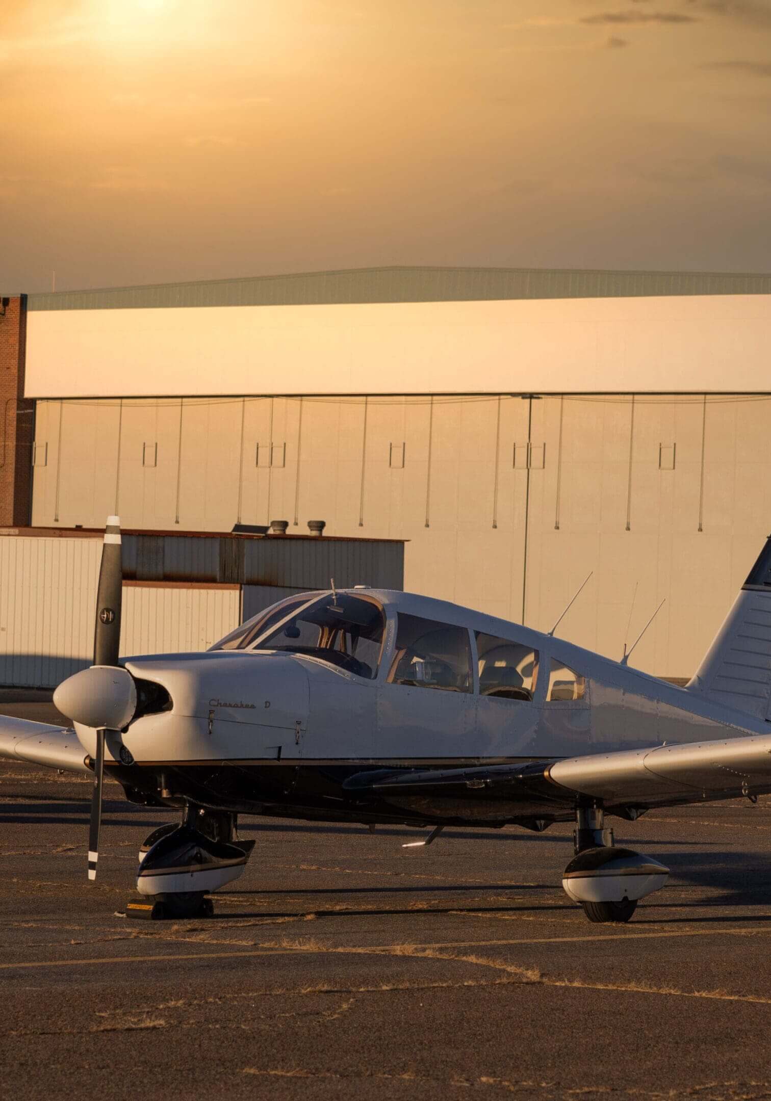 Small airplane parked near large hangars.